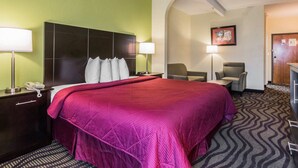 Ein Hotelzimmer mit einem großen Bett, zwei Nachttischen mit Lampen, einem Sessel und einem Schreibtisch.