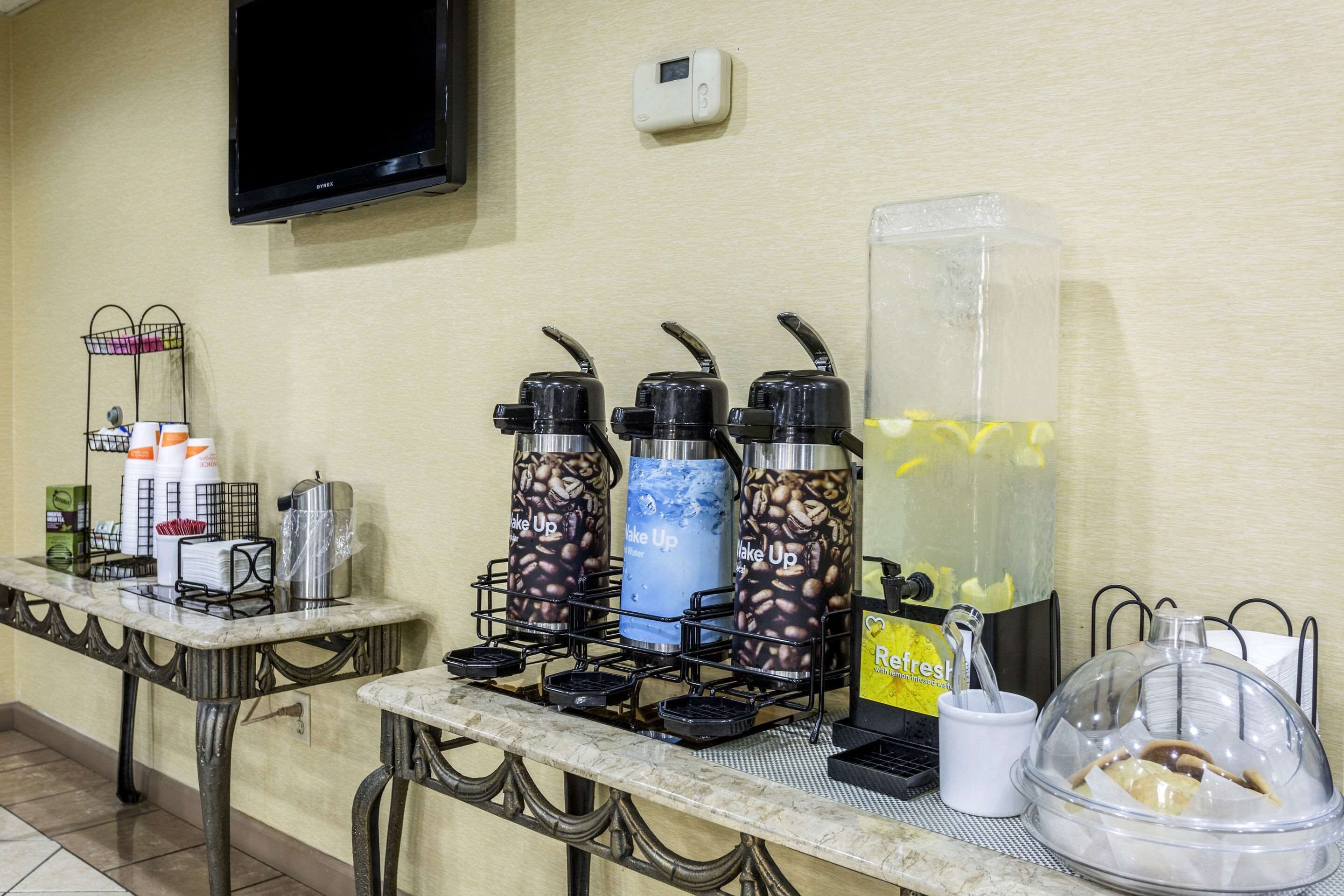 Un angolo dedicato alle bevande self-service con distributori di caffè e tè, un dispenser d'acqua e un contenitore termico di grandi dimensioni con canuccia.