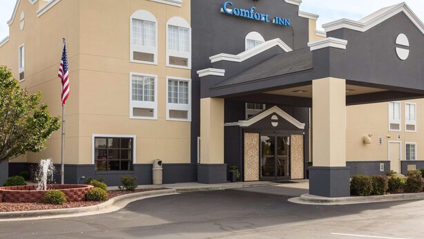 A Comfort Inn hotel with a beige facade, a flag, and a fountain.