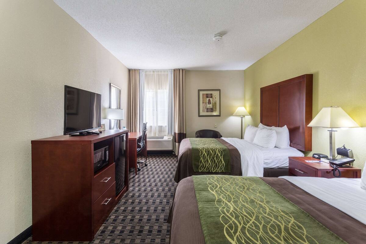 A hotel room with a bed, a desk with a television, a chair, a desk lamp, and a window with curtains.
