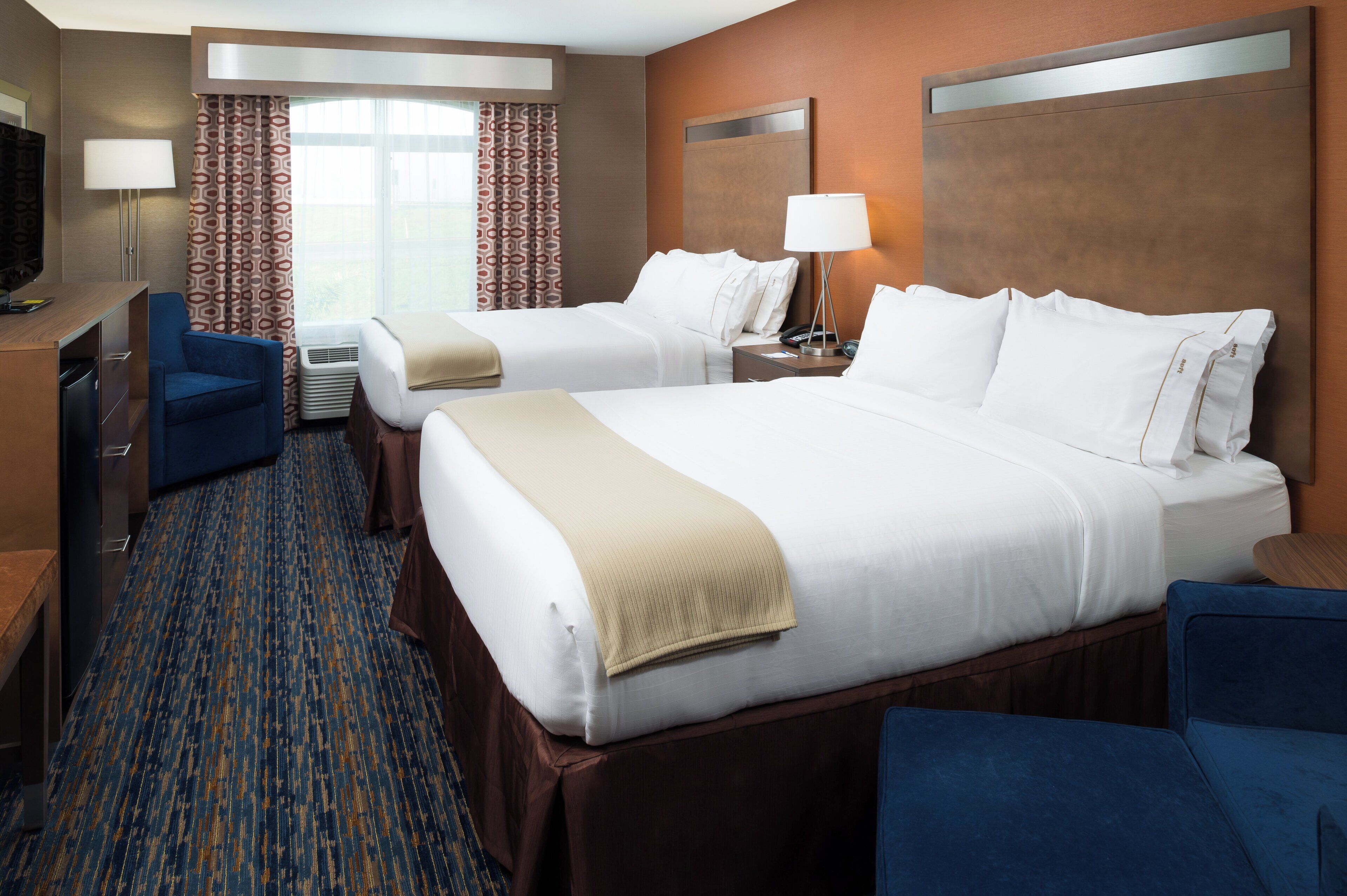 A hotel room with two beds, a desk, a chair, a TV, and a window with curtains.