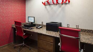 A hotel room with a desk, two red chairs, a computer, and a printer.