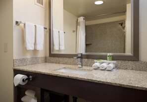 A bathroom with a granite countertop, a sink, a mirror, and a shower visible in the reflection. - Holiday Inn Express Rocklin - Galleria Area by IHG (Rocklin)