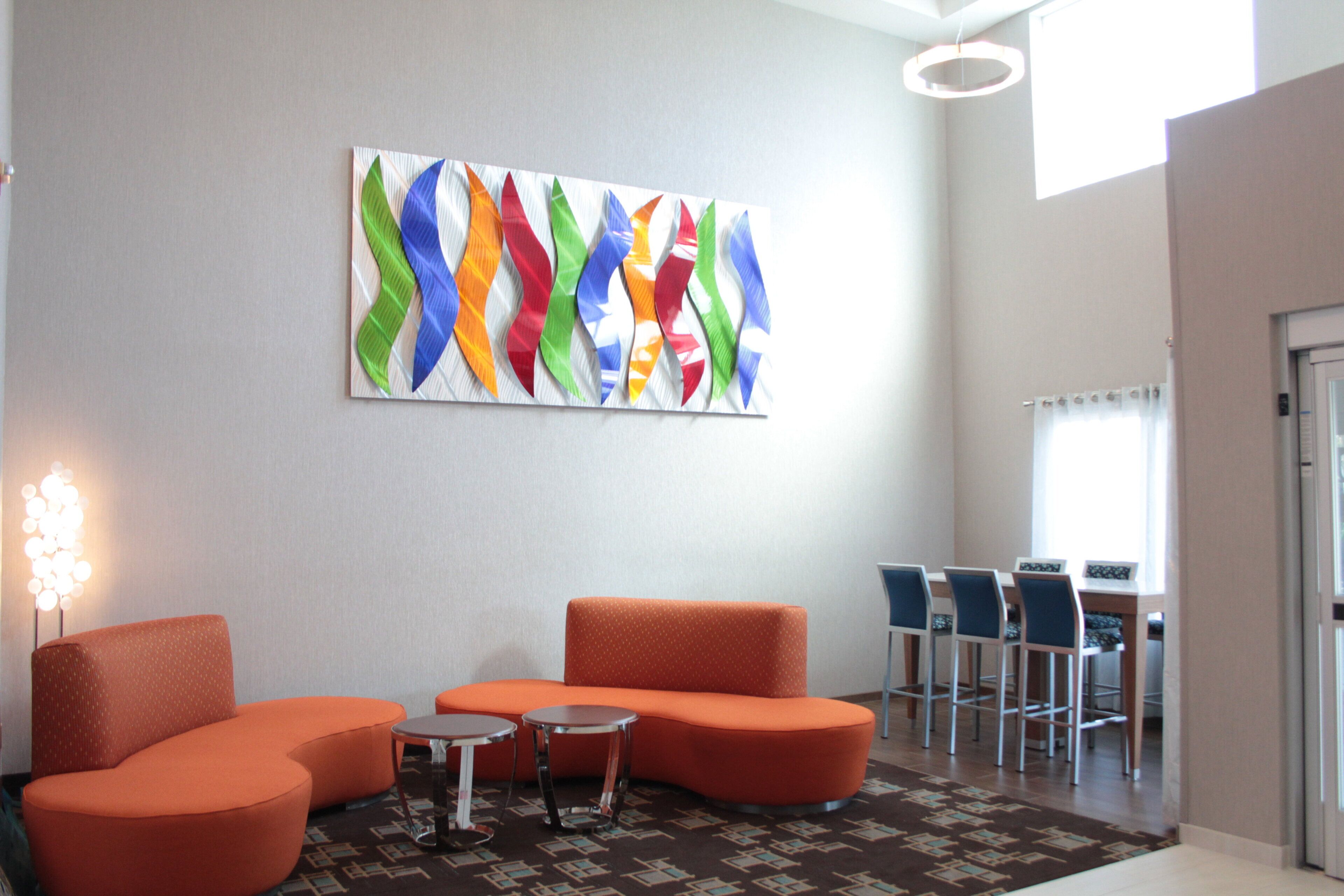 Un hall d’entrée avec des sièges orange, une petite table et un tableau abstrait aux couleurs vives accroché au mur.