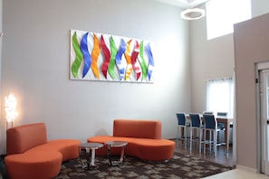 A lobby with orange seating, a small table, and a colorful abstract painting on the wall. - Holiday Inn Express Rocklin - Galleria Area by IHG (Rocklin)
