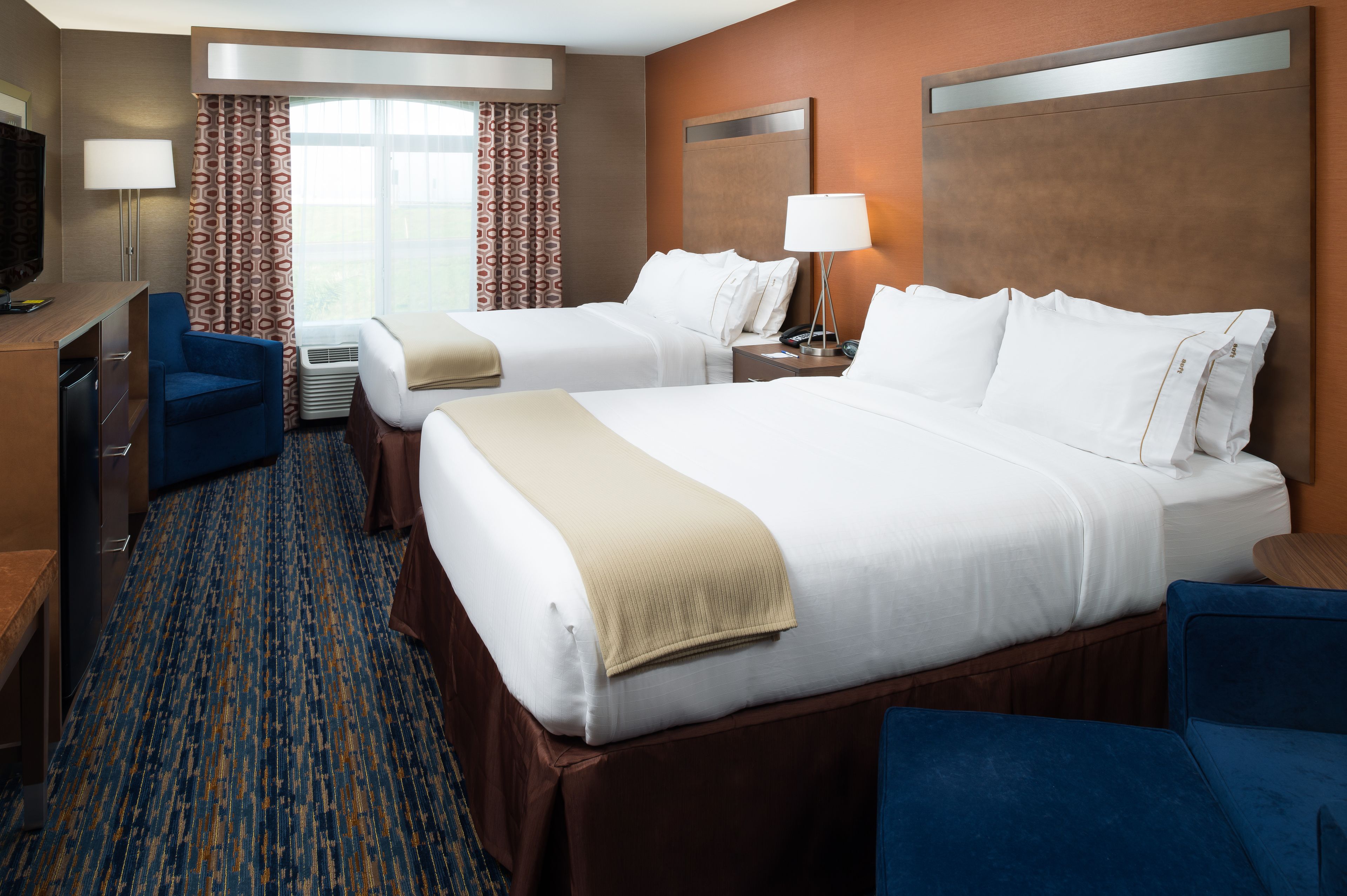 A hotel room with two beds, a desk, a chair, a TV, and a window with curtains.