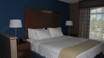 A hotel room with a large bed, two bedside tables with lamps, a wooden headboard, and a window with patterned curtains.
