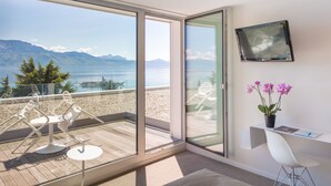 Un balcón con vista al mar y a las montañas, un escritorio blanco con una silla, y una orquídea en maceta.