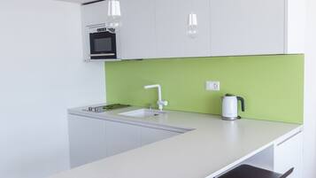 A modern kitchen with a white countertop, green backsplash, and a built-in oven. There are two bar stools and a white sink.