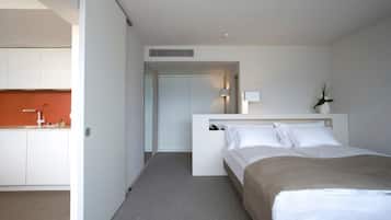 Una habitación de hotel moderna con una cama, una mesita de noche, una lámpara y vistas a la cocina.