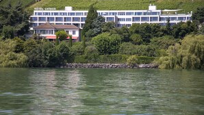 Un hotel llamado HOTEL LAVAUX con diseño moderno, situado junto a una masa de agua, rodeado de exuberante vegetación.