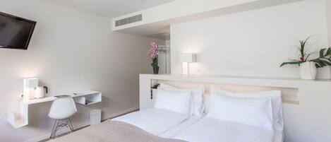 Una habitación de hotel moderna con una cama, un escritorio con silla, un televisor montado en la pared y una planta en maceta.