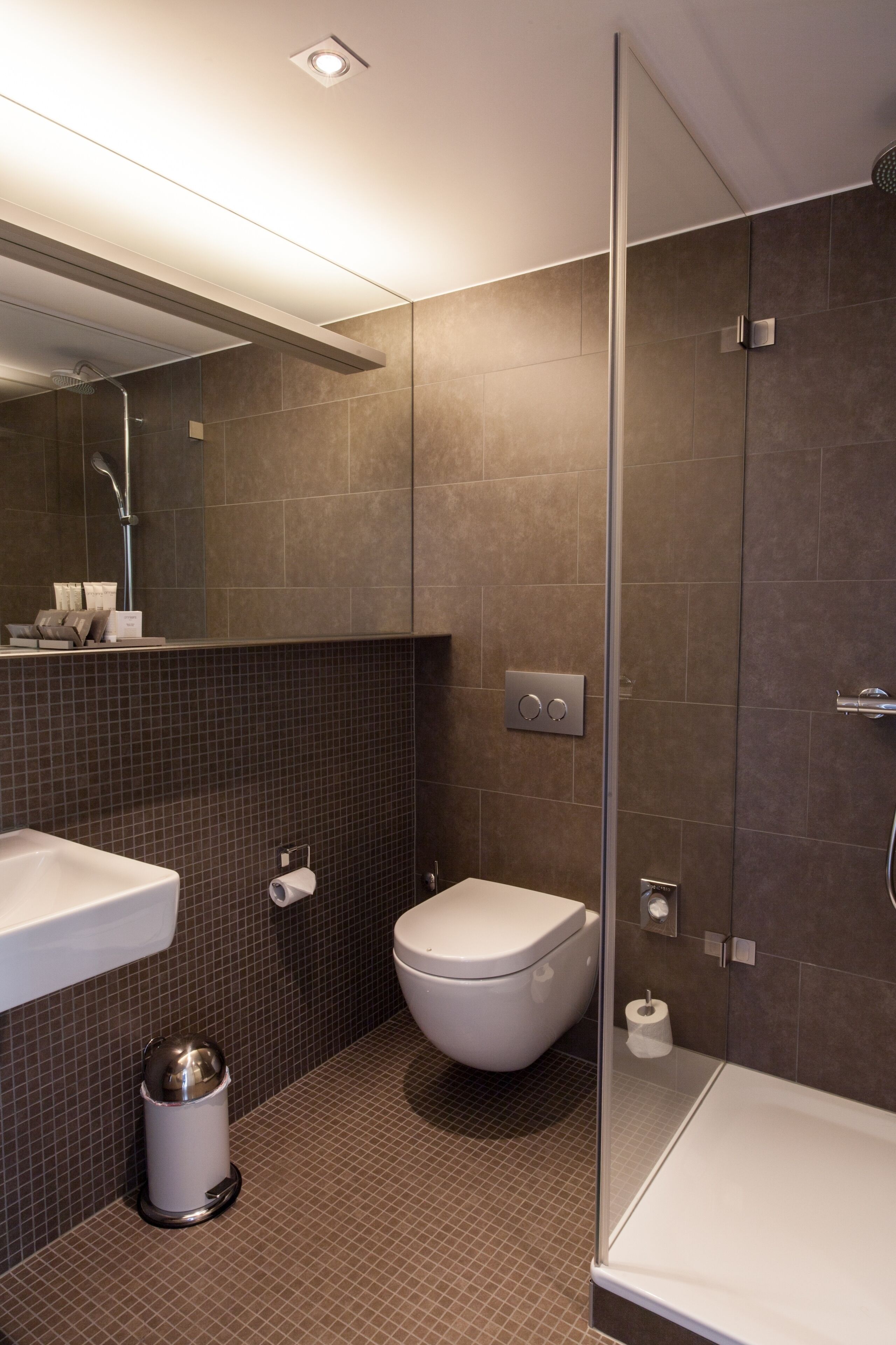 Un baño moderno con cabina de ducha de vidrio, un lavabo blanco y un inodoro.
