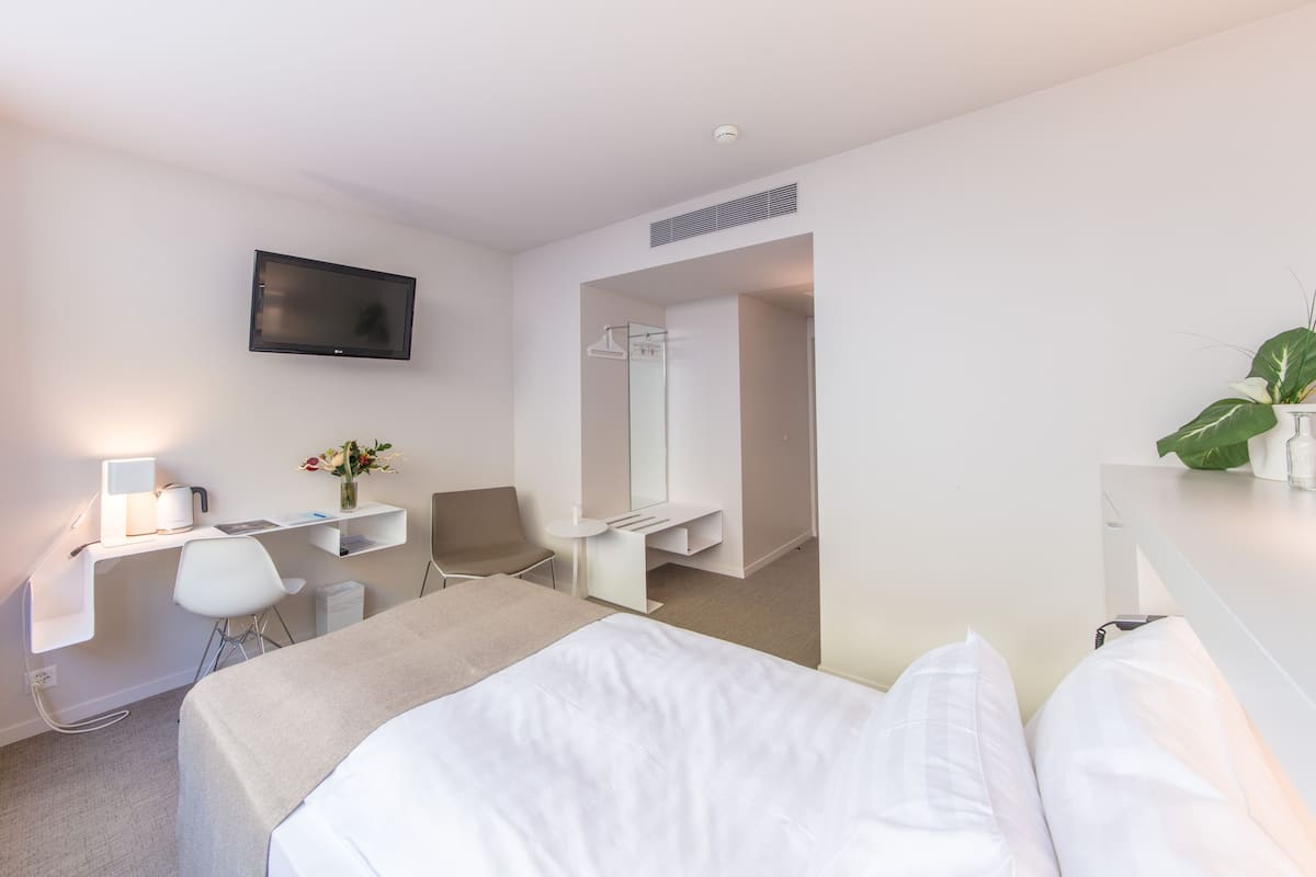 Een moderne hotelkamer met een bed, een bureau met een computer, een stoel, een aan de muur bevestigde televisie en een spiegel.