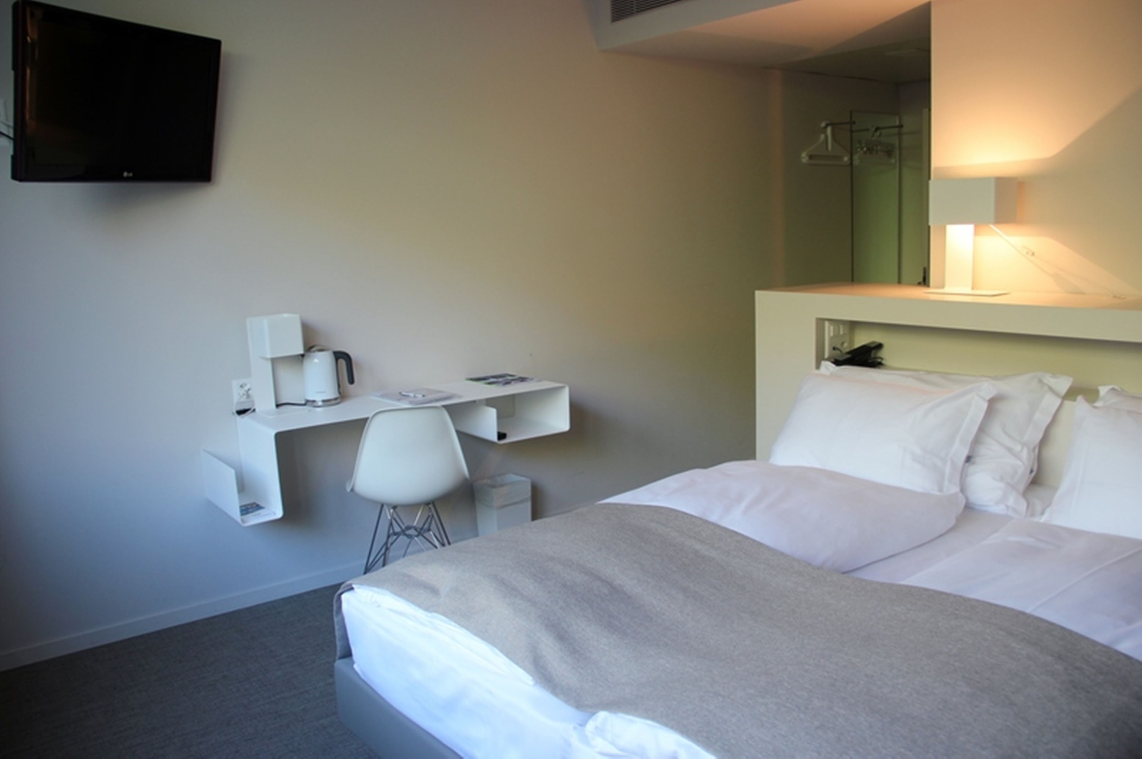 A hotel room with a bed, a desk with a chair, a television, and a mirror.
