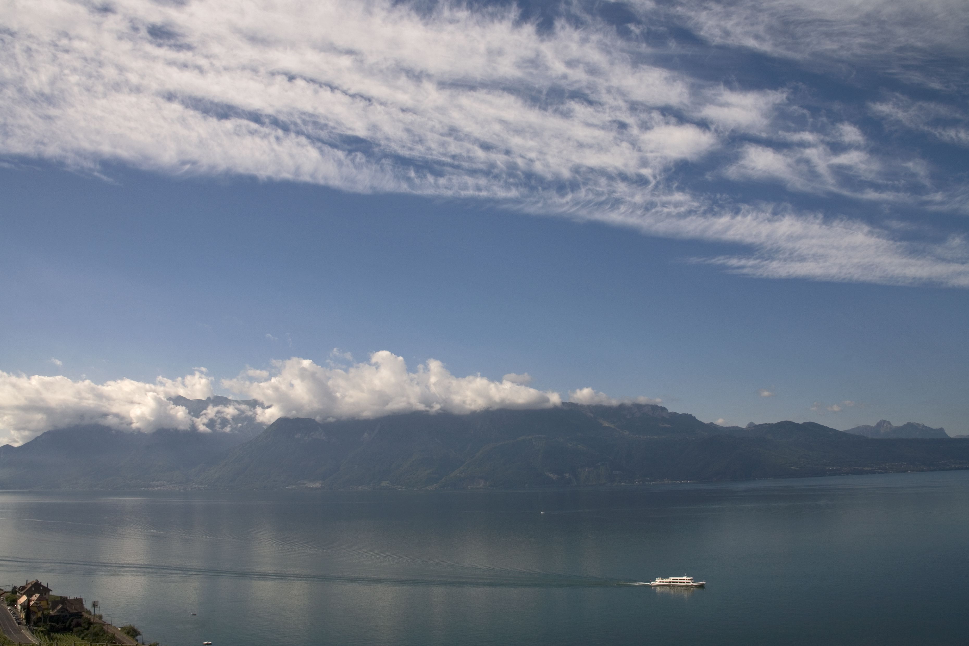 A calm lake with a boat, mountains in the background, and a clear sky.