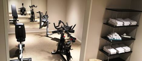 A home gym with exercise equipment, a mirror, and a shelf with folded towels.