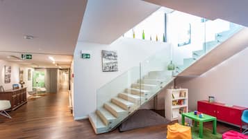 A modern interior with a glass staircase, wooden flooring, a green table, and a red cabinet.