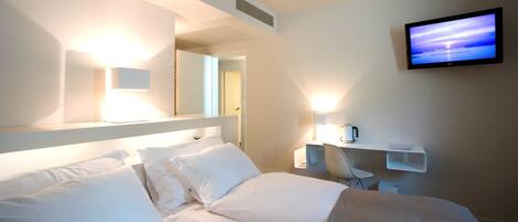 A hotel room with a bed, a TV mounted on the wall, a coffee machine, and a chair.
