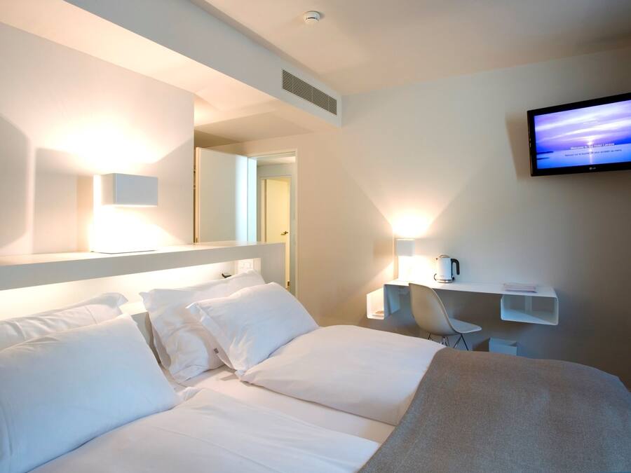A hotel room with a bed, a TV mounted on the wall, a coffee machine, and a chair.