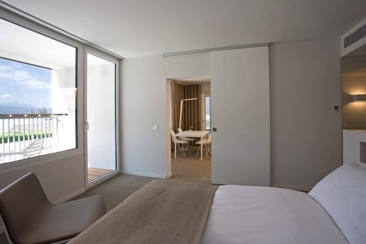 Hotelkamer met een groot bed, een zithoek met een stoel, een balkon met uitzicht en een aparte eethoek.
