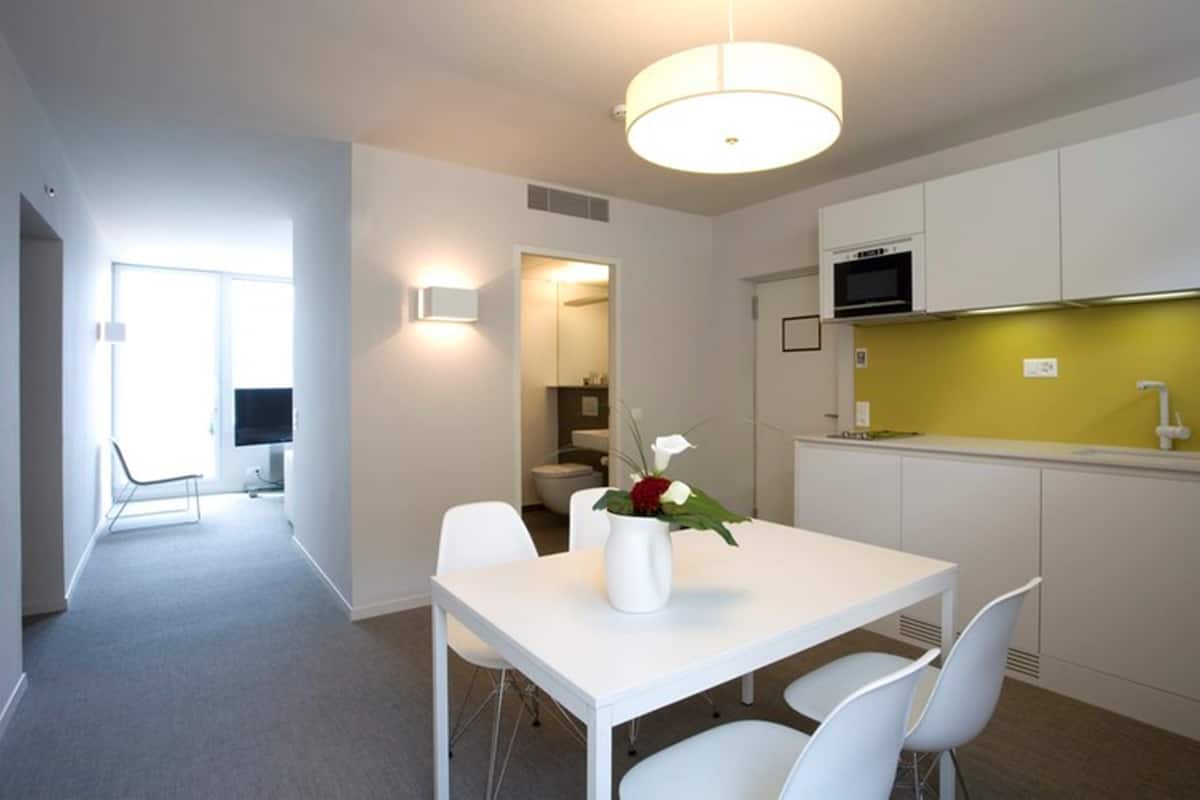 Een moderne keuken met witte kasten, een gele spatwand, en een eethoek met een witte tafel en stoelen.