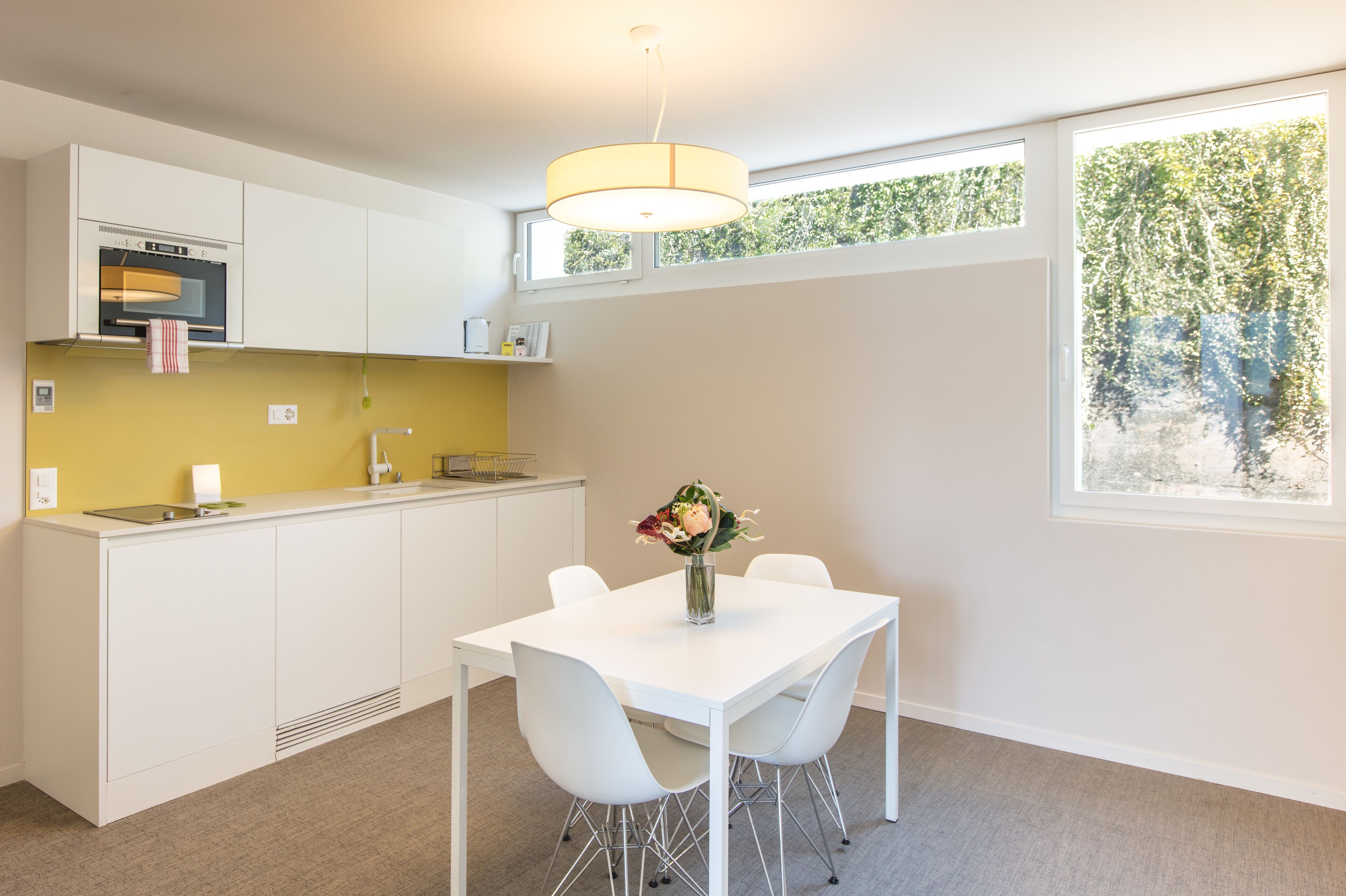 A modern kitchen with white cabinetry, a built-in oven, and a window with a view of trees.