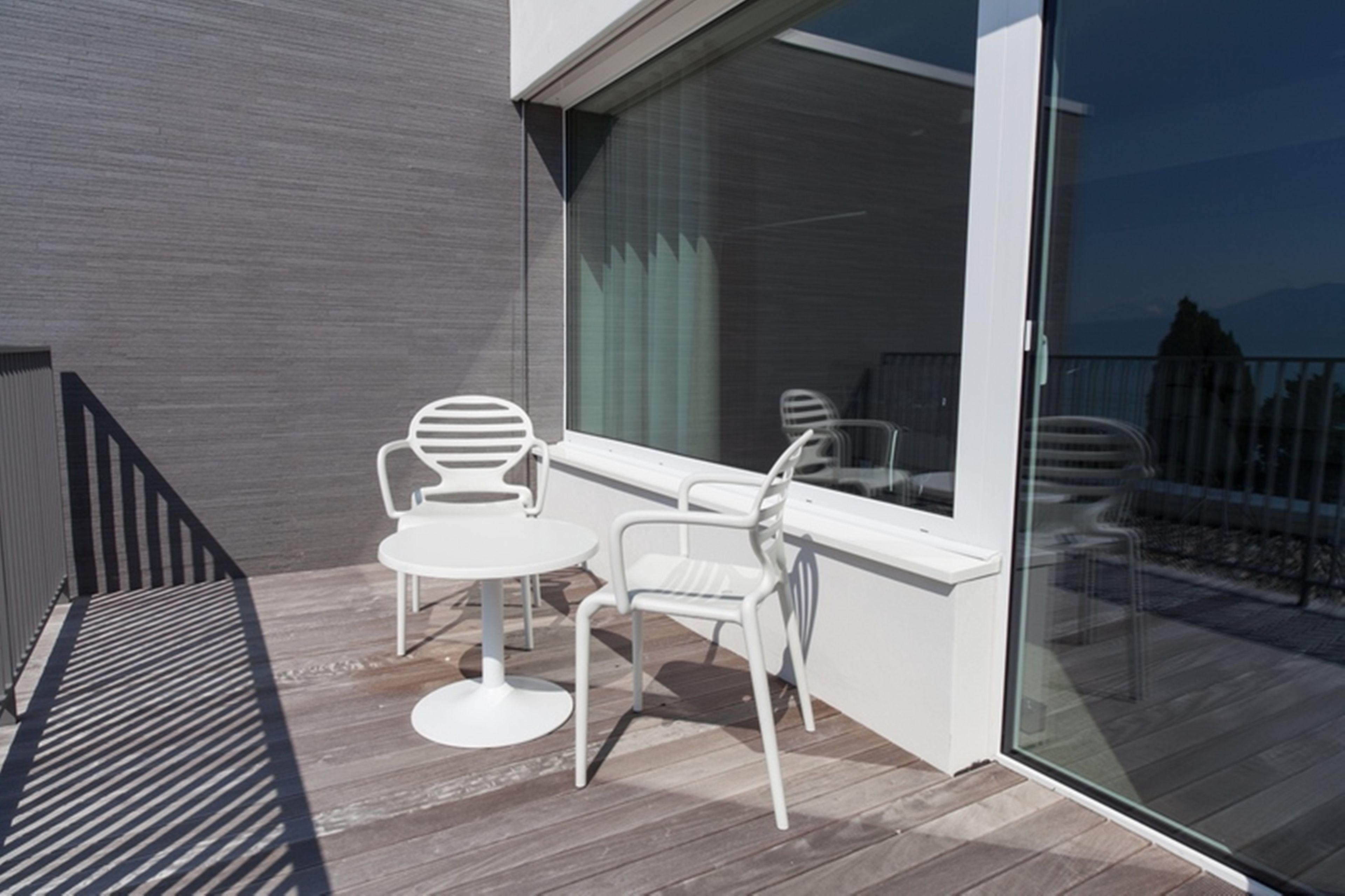Un balcon moderne donnant sur l’extérieur, avec des meubles blancs, notamment une table ronde et deux chaises, et une porte vitrée qui mène à une terrasse.