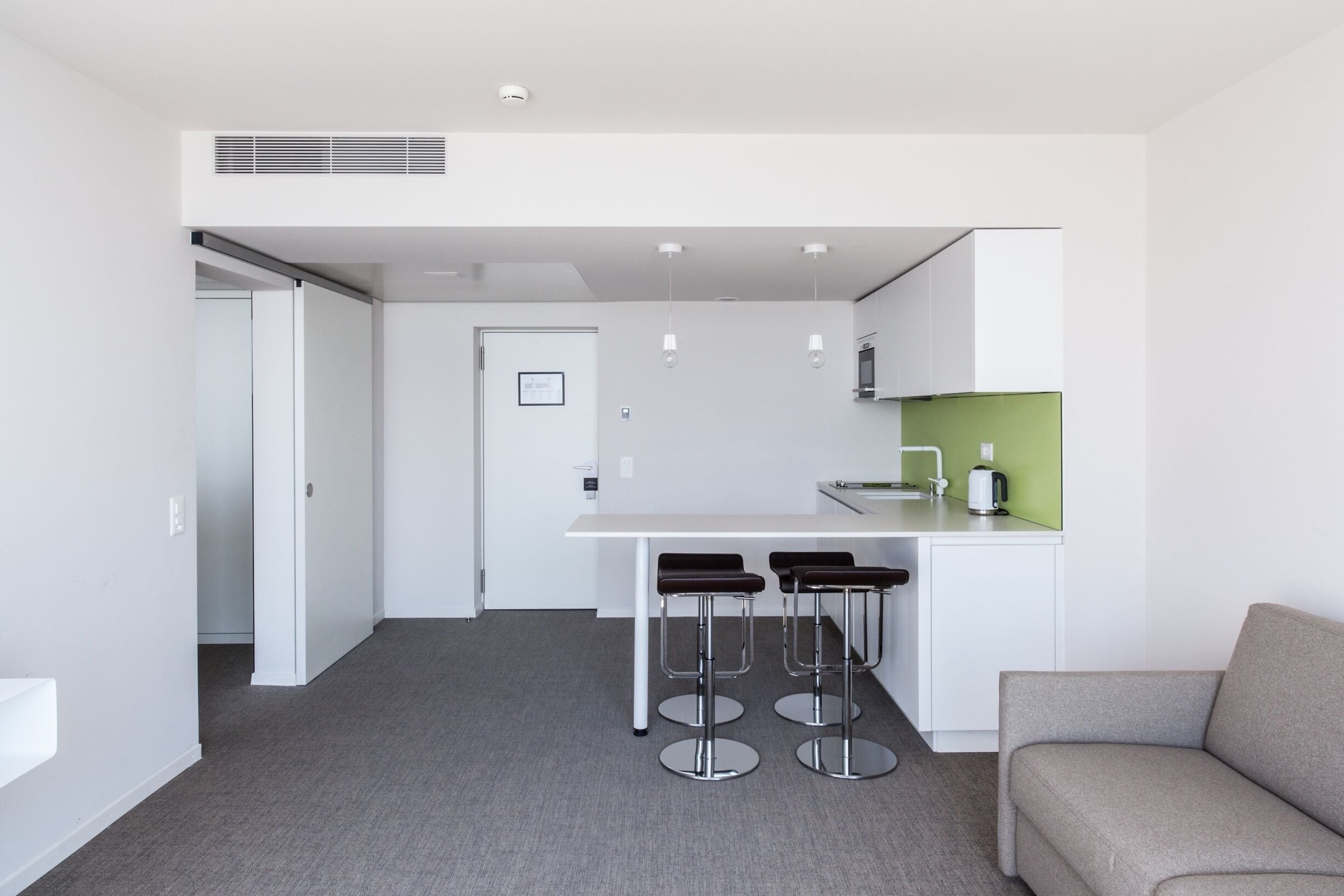 A modern kitchen with a white countertop, a green backsplash, and a bar stool seating area.