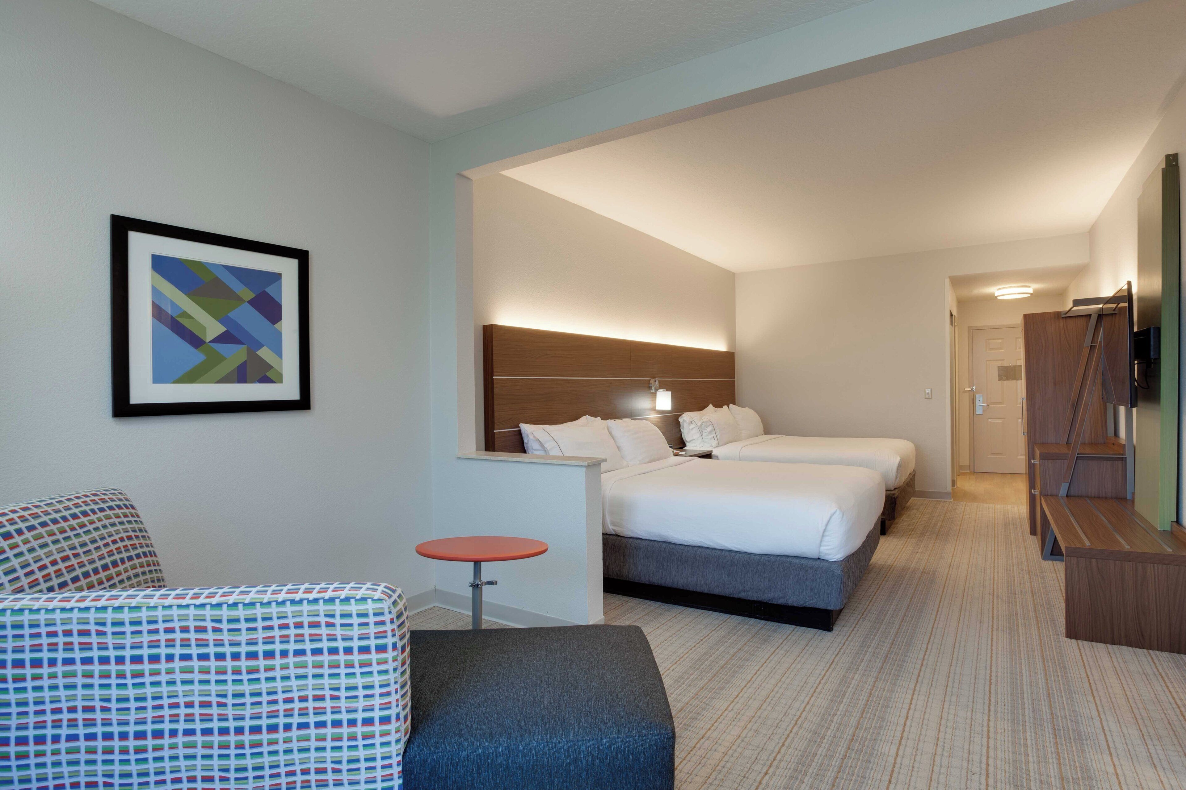 Quarto de hotel com cama, mesas de cabeceira, mesa redonda pequena, sofá e quadro na parede.