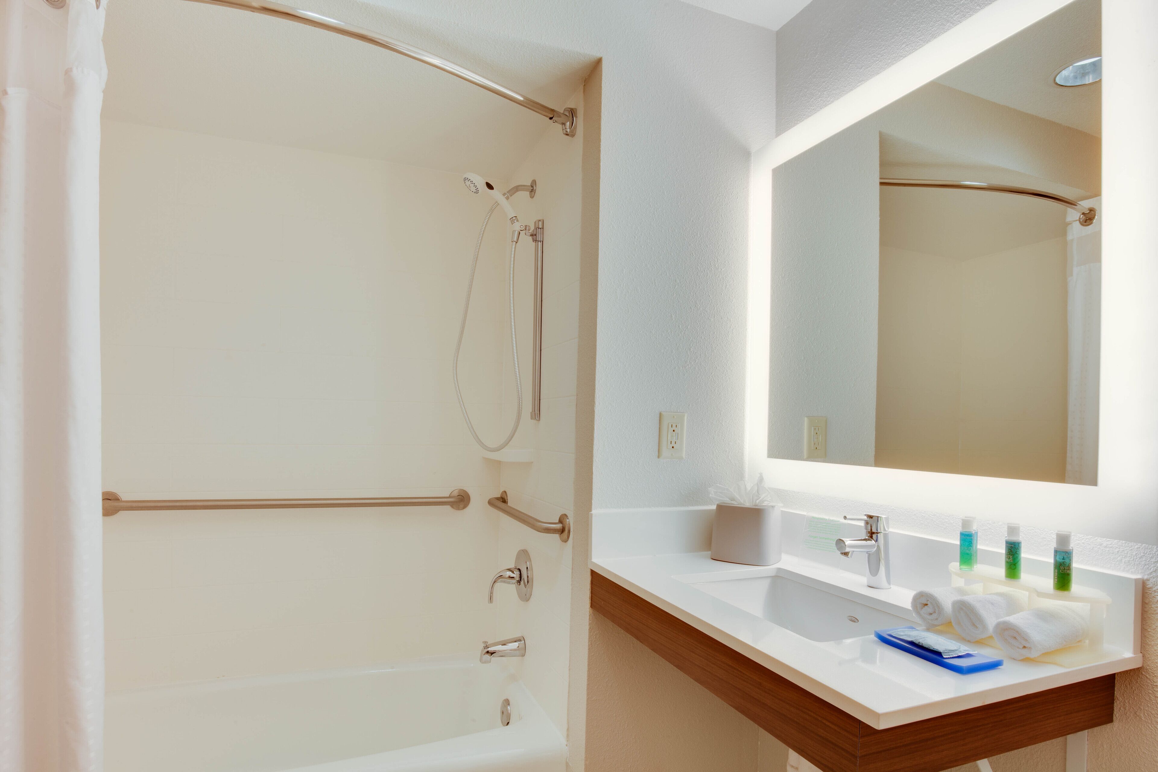 A bathroom with a bathtub, a shower, a sink with toiletries, and a mirror.