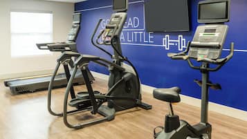 Ein Fitnessraum mit Laufbändern und Crosstrainern, eine blaue Wand mit motivierenden Texten und ein Fenster mit Tageslicht.