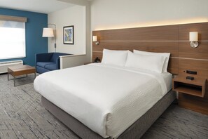 A hotel room with a large bed, a desk, a chair, and a wall-mounted lamp.