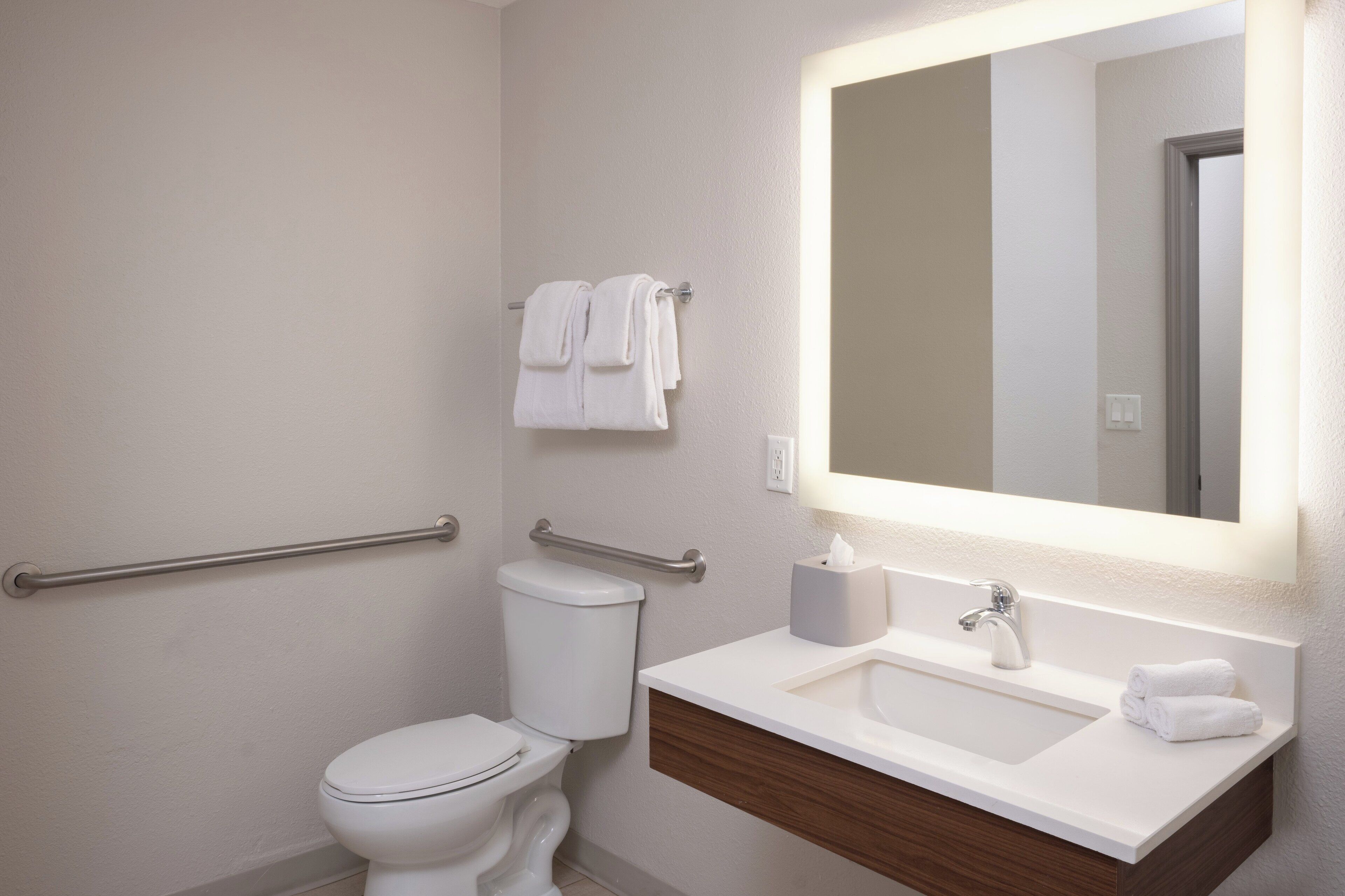Un baño moderno con inodoro blanco, lavamanos con espejo y toallero con toallas.