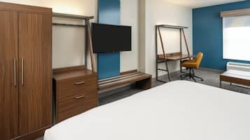 A hotel room with a large bed, wooden wardrobe, a desk with a chair, a TV mounted on the wall, and a window.