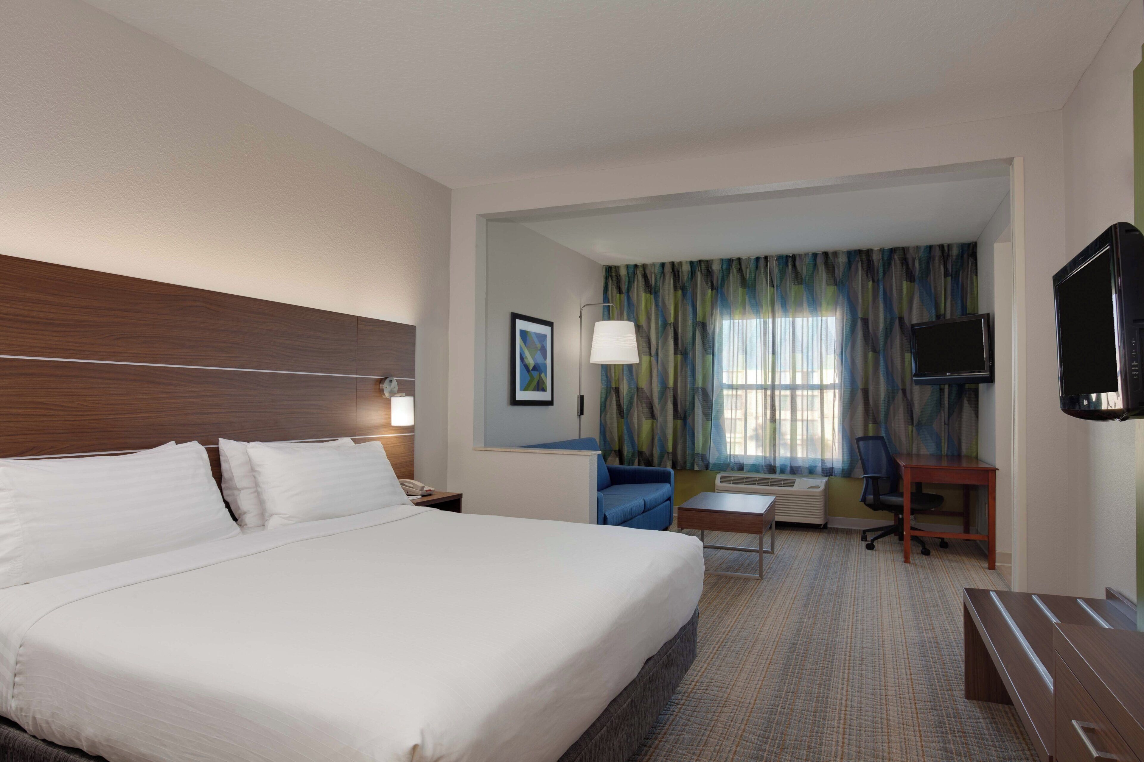 A hotel room with a large bed, a desk, a chair, a television, and a window with curtains.