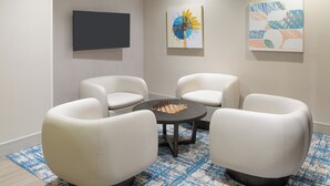 Una habitación moderna con cuatro sillas blancas alrededor de una mesa central, un televisor de pantalla plana en la pared y dos cuadros abstractos.