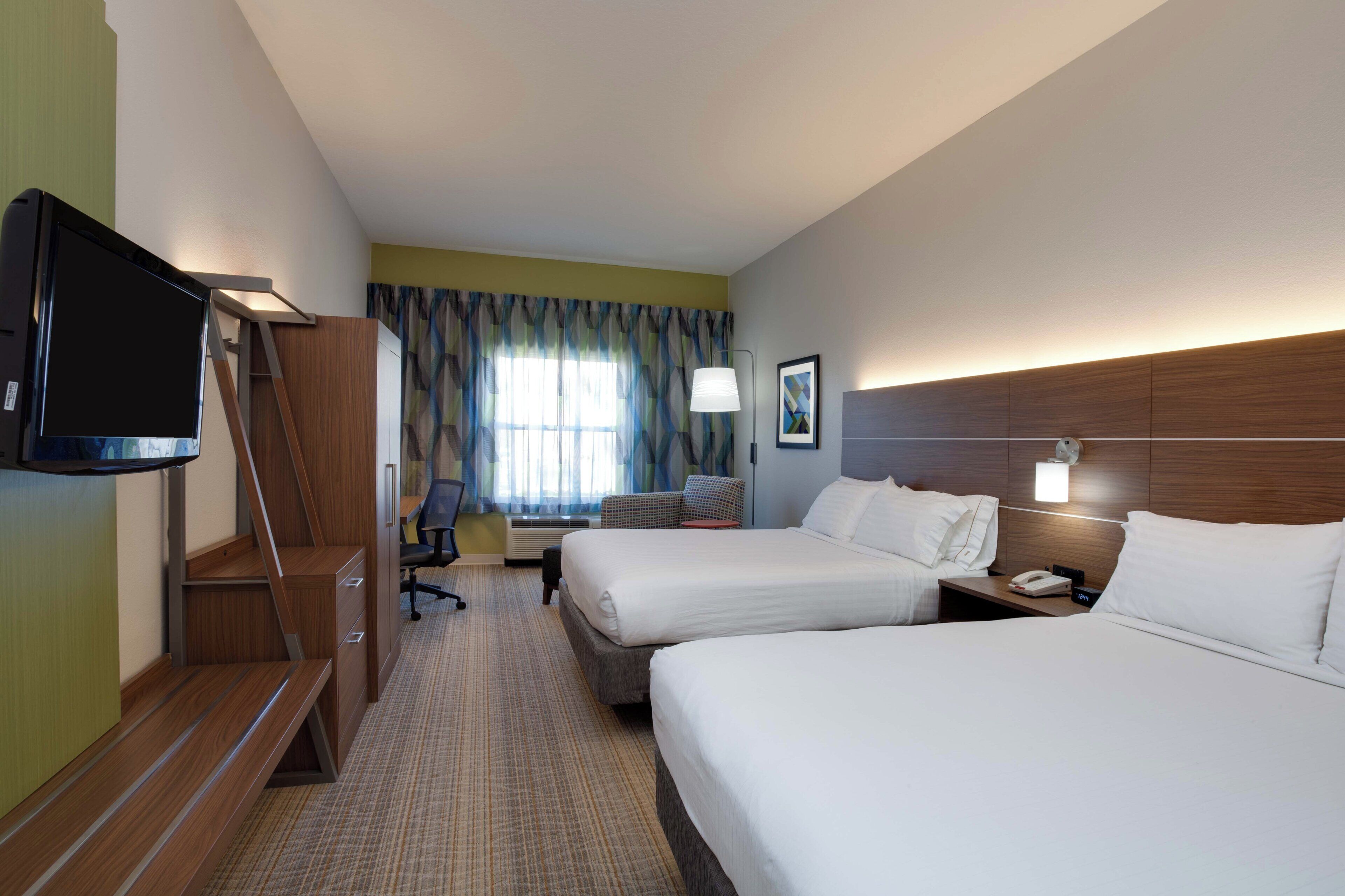 A hotel room with two beds, a desk, a chair, a television, and a window with curtains.