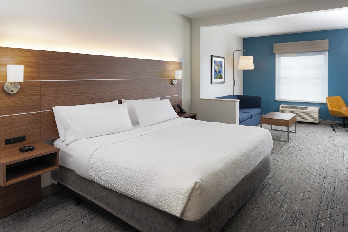 Une chambre d’hôtel avec un grand lit, des tables de chevet, un bureau, une chaise et une fenêtre avec des stores.