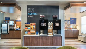 Una estación de café con cafeteras espresso, un dispensador de yogur y una exhibición de frutas.