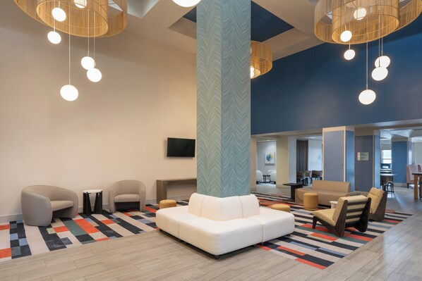 Un hall d’entrée moderne avec des espaces de détente, un pilier décoré et des luminaires suspendus.