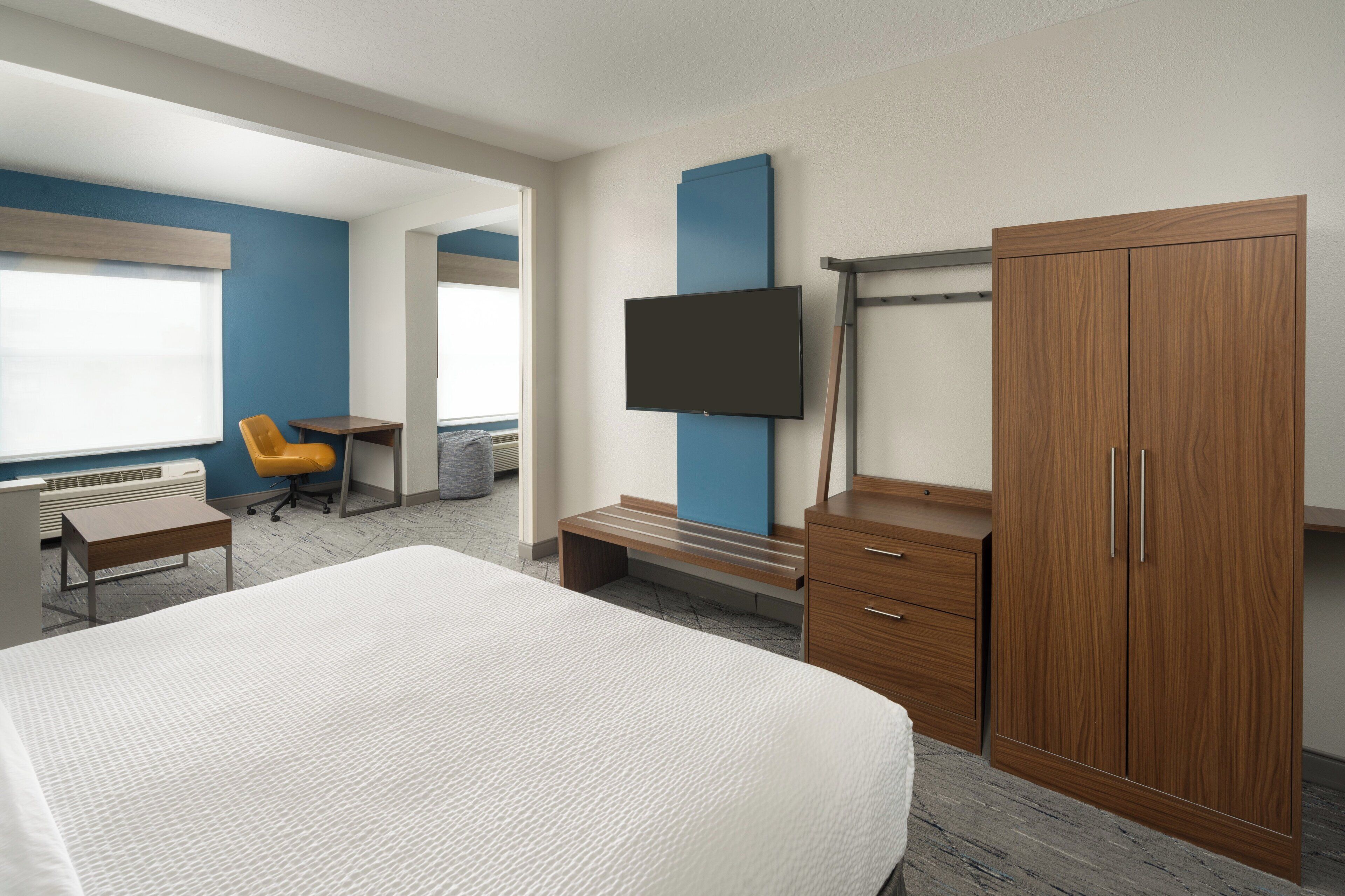 A hotel room with a large bed, a desk with a chair, a TV mounted on the wall, and a wardrobe.