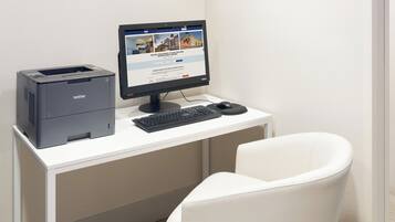 A Brother printer and monitor on a white desk with a white chair.