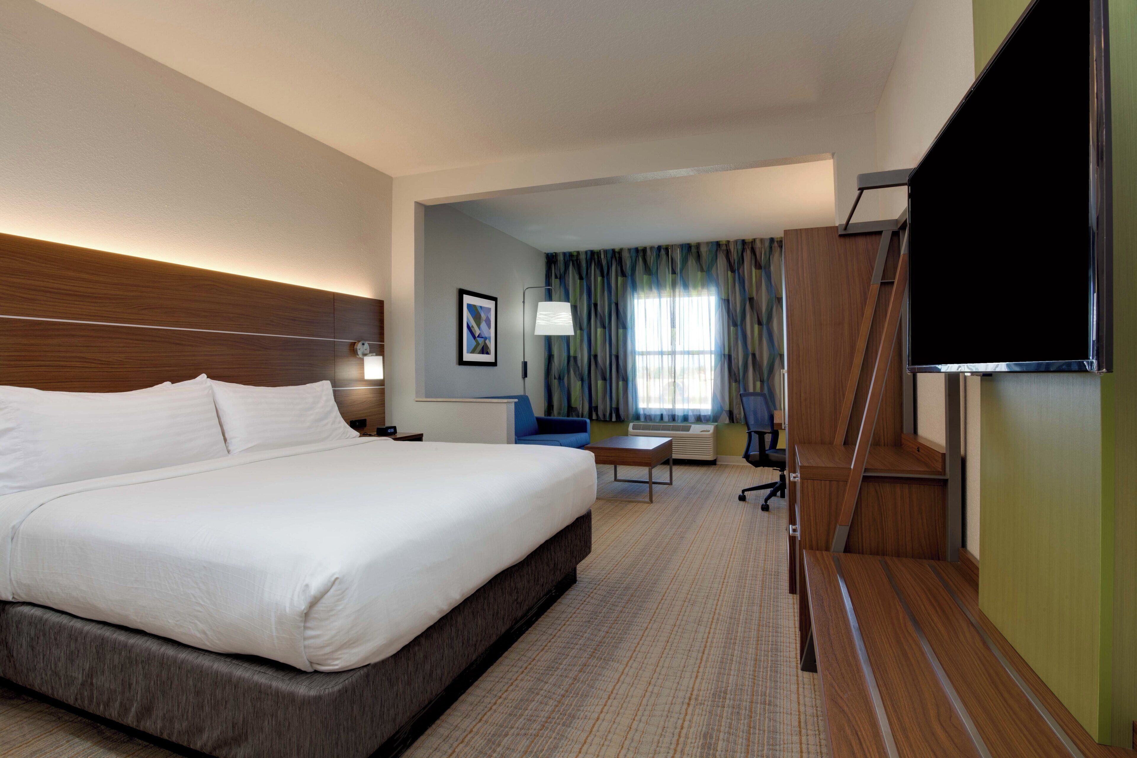 A hotel room with a large bed, a desk, a chair, a flat-screen TV, and a window with curtains.