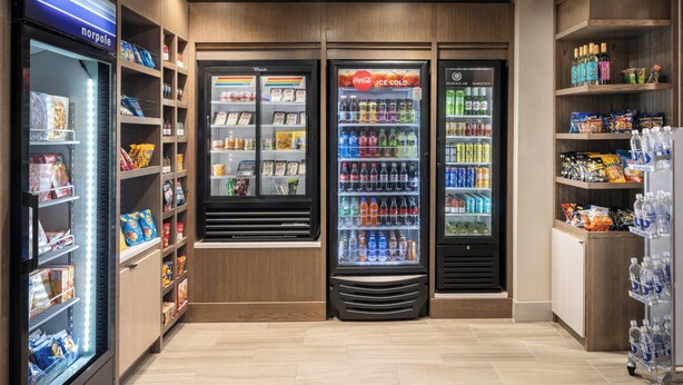 Un área de bebidas autoservicio con dispensadores refrigerados, estantes de snacks y un enfriador de agua.