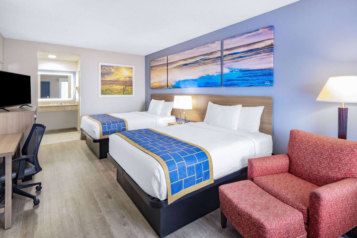 Une chambre d’hôtel avec deux lits, un bureau, une télévision et des œuvres d’art accrochées aux murs.