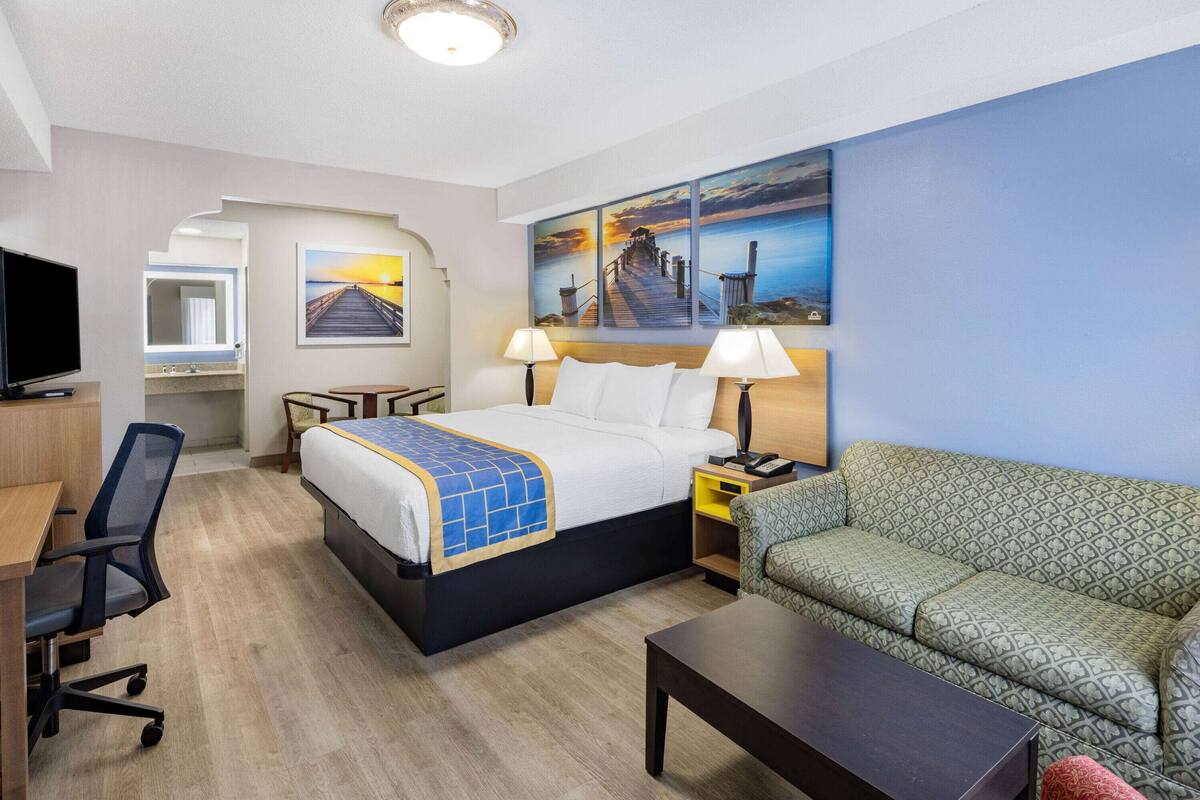 Une chambre d’hôtel comprenant un lit, un bureau, une télévision, un canapé et un tableau représentant une jetée.
