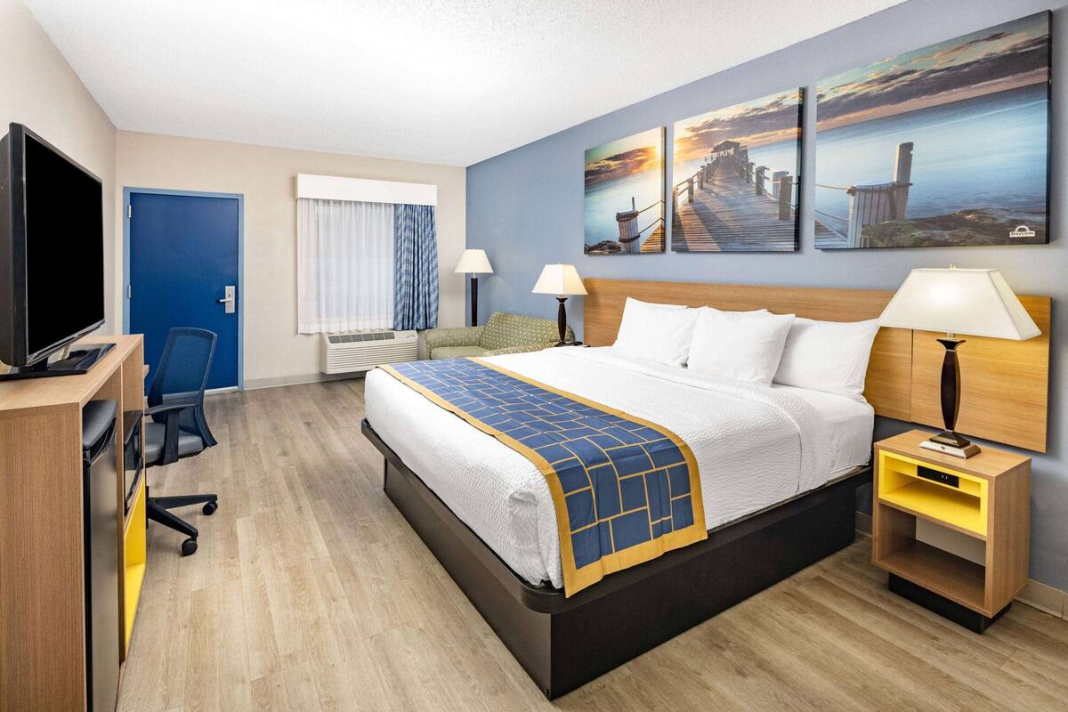 Une chambre d’hôtel équipée d’un lit, d’un bureau, d’une télévision et ornée d’œuvres d’art au mur.