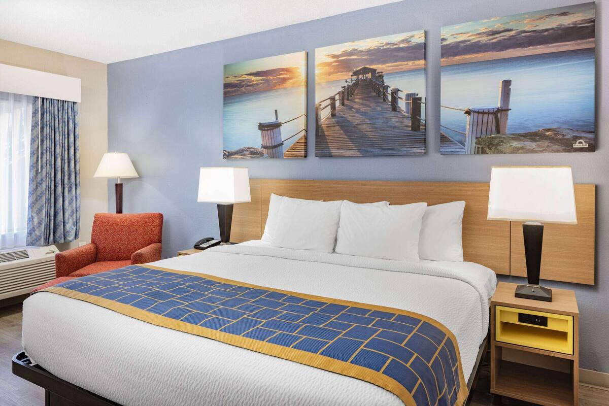 Une chambre d’hôtel avec un lit, deux tables de chevet, une chaise et trois tableaux accrochés au mur.