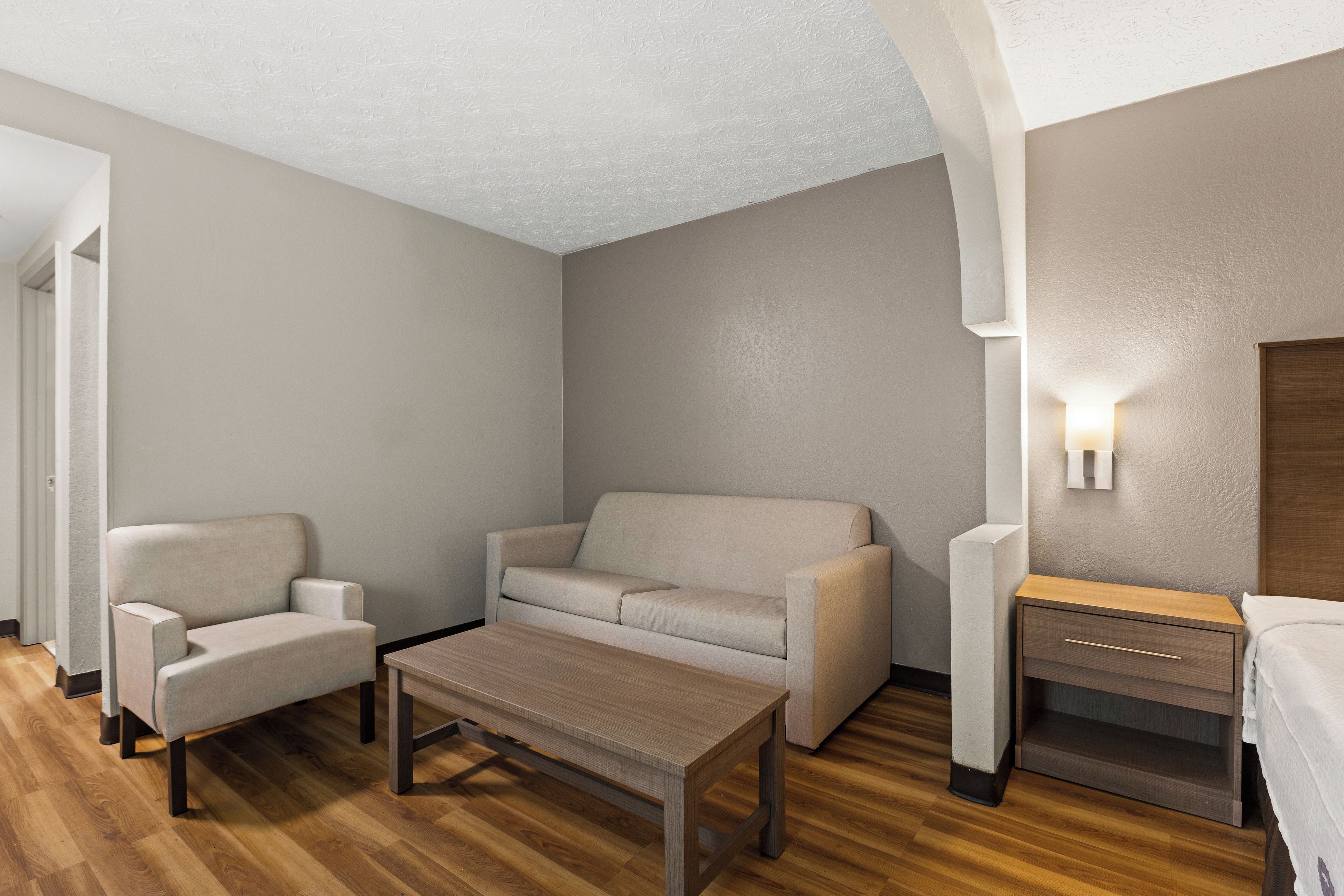 Habitación de hotel moderna con sofá, sillón, mesa de centro de madera y mesita de noche con lámpara.